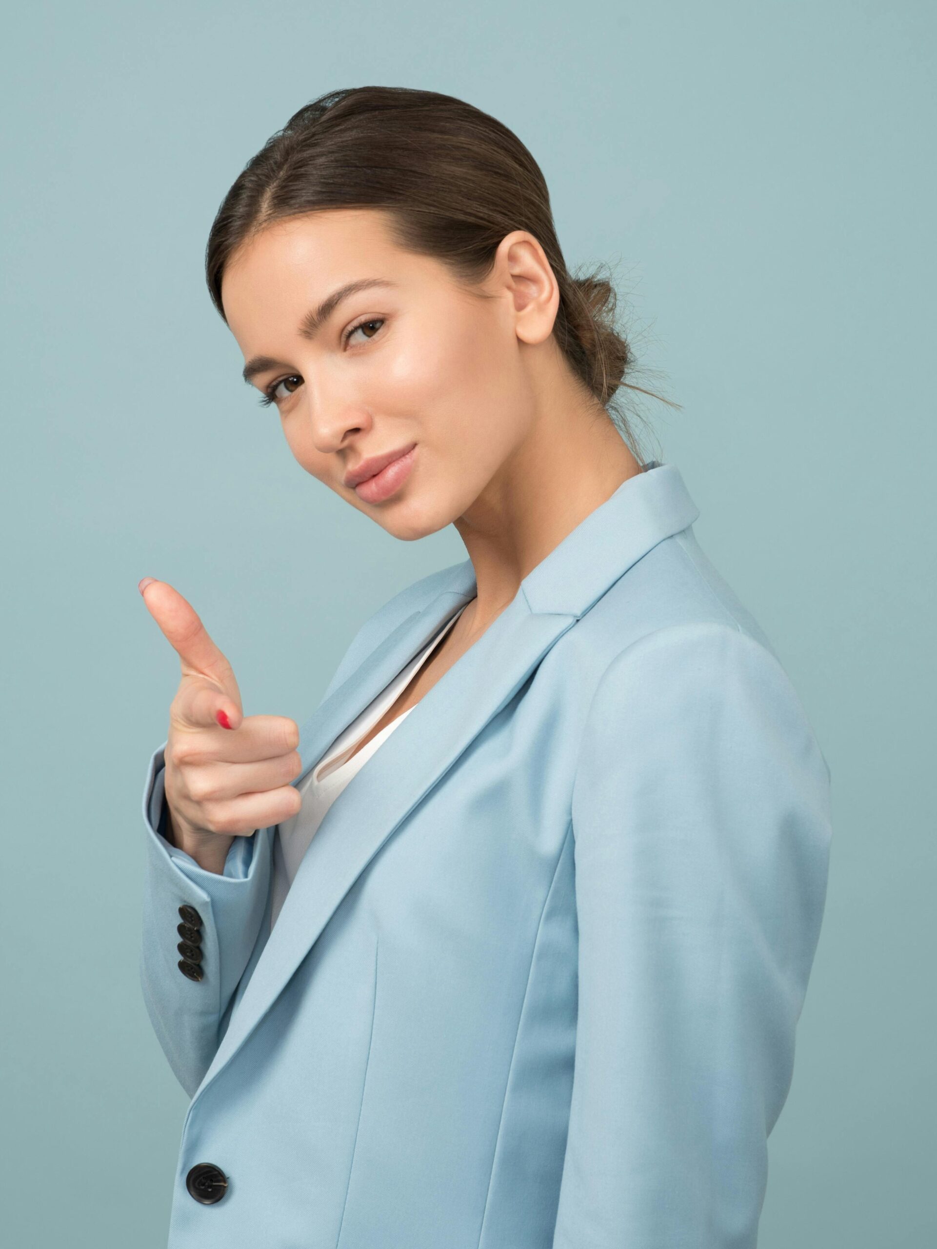 A young woman in a blue suit exhibits confidence with a relaxed pose against a blue background.