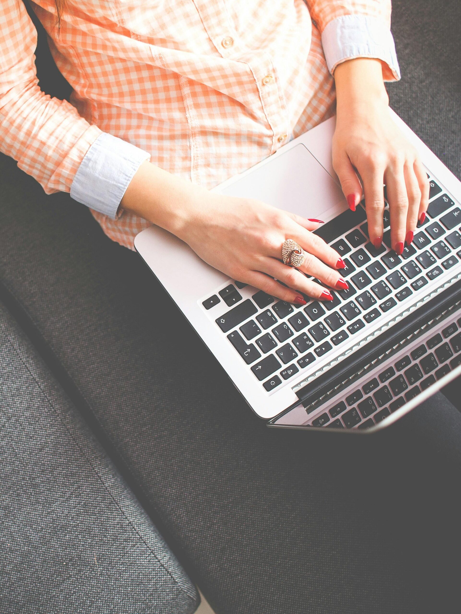A woman typing on a laptop, sitting on a sofa in casual attire, viewed from above.